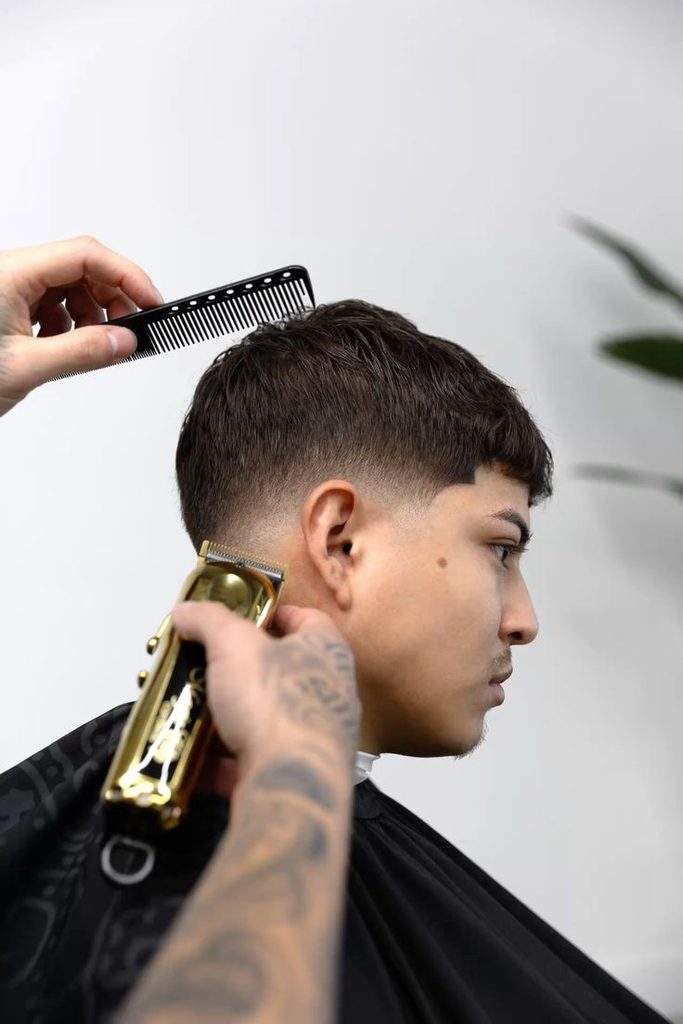 Barbero realizando un corte degradado en barbería latina moderna.