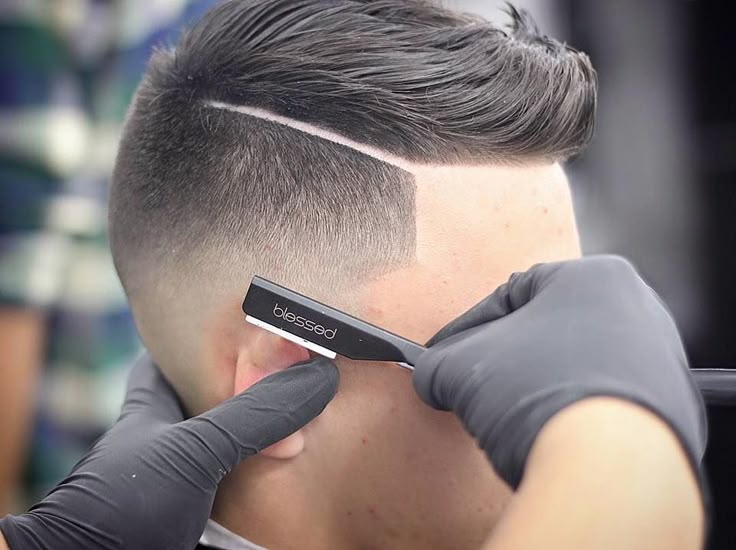 Barbero perfilando con navaja un diseño de grecas en corte degradado para hombre.